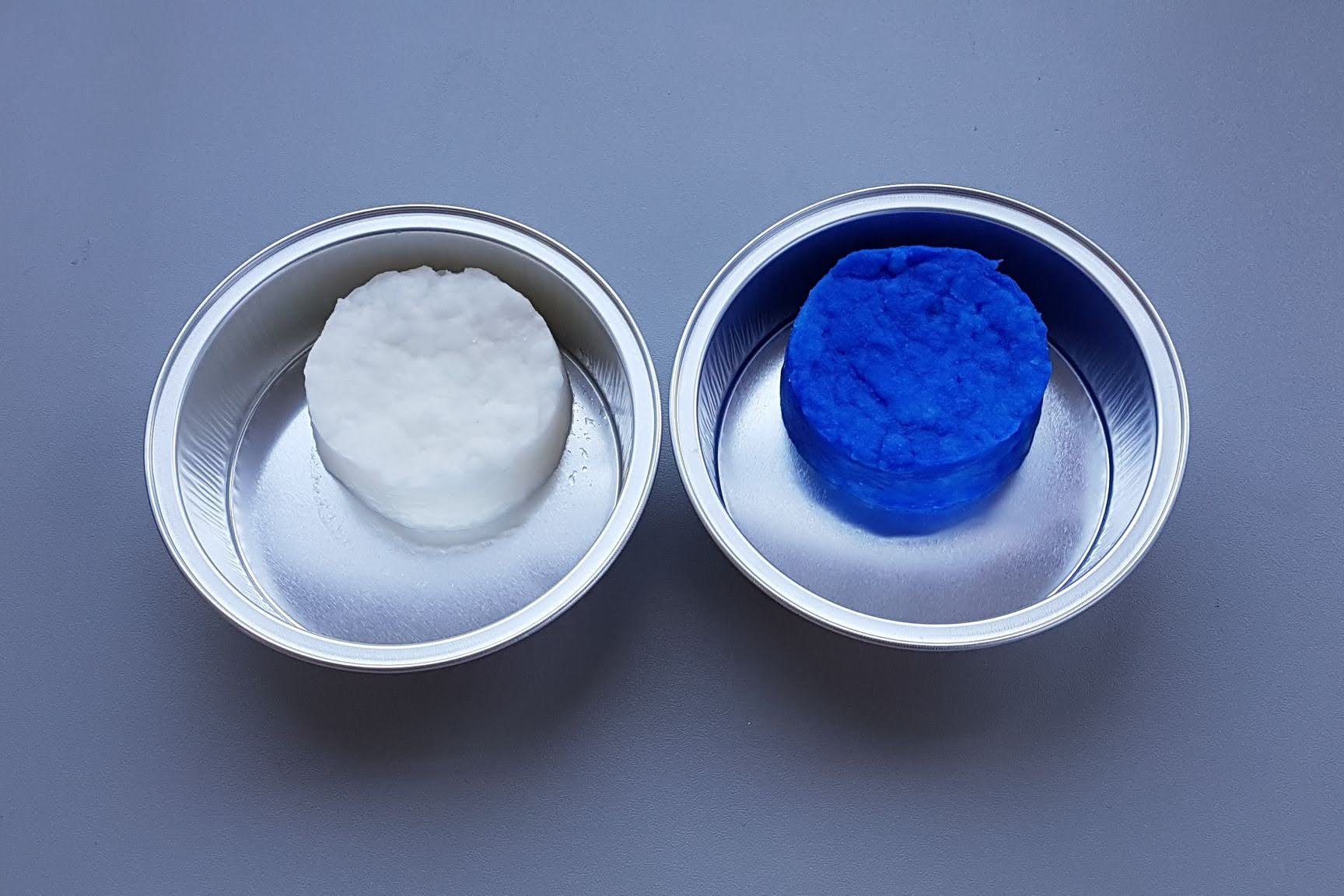 Two filter cake pucks side by side in stainless dishes, one washed white and one unwashed blue, showing cake wash efficiency